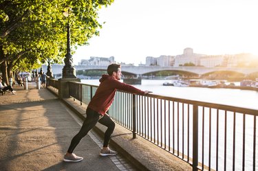 Young sporty man with earphones stretching on a railing outside in a London city.