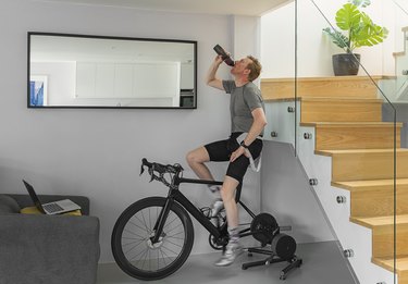 caucasian man drinking from water bottle while working out on a stationary bike at home