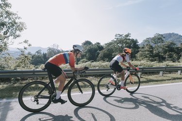 Two cyclists wearing helmets biking on the side of a road