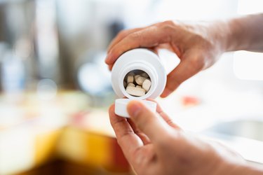 Close-up of hands pouring vitamin C supplements out of bottle and into hand