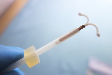 Fingers in blue glove holding IUD over blue background