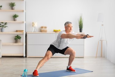 Older adult wearing a white T-shirt and black shorts doing a side lunge as part of a low-impact Tabata workout.