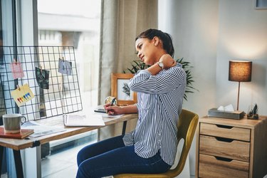 A woman rubs her neck at her desk