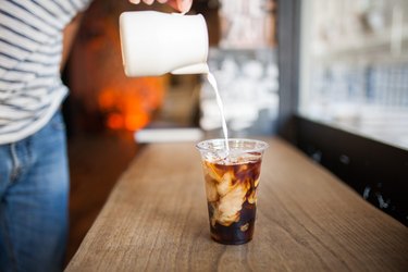 person pouring healthy coffee creamer into cold brew coffee on a wooden table