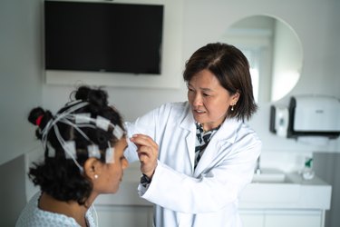 A doctor in a white lab coat placing electrodes on a person's head so they can prepare for a sleep study