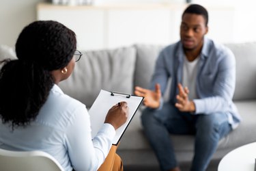 Man sitting on grey couch talking to therapist with notepad