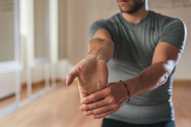 Sporty man stretching forearm before gym workout