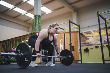 Person wearing black sports bra and leggings doing a deadlift in the gym with a barbell.