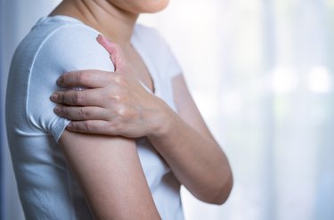 close up of a caucasian woman in white shirt holding her sore shoulder