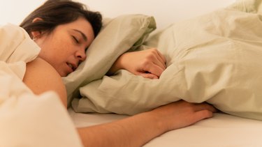 person with long brown hair talking in their sleep on their tan pillows and sheet set