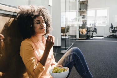 Young woman having a break in office with a bowl of grapes