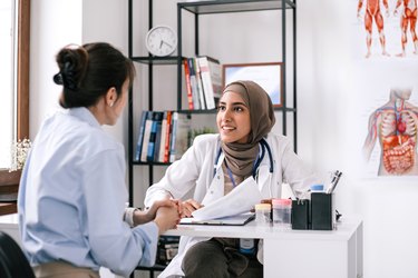Close up of a doctor in a white coat talking to a patient in their office, to help reduce the patient's white coat syndrome