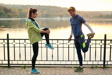 fit couple performing mobility exercises for runners by the water before their run