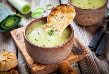 homemade cream of leek soup with croutons in bowl on wooden board