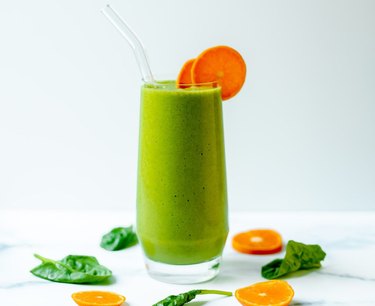 Vibrant green smoothie in a clear glass garnished with orange slices
