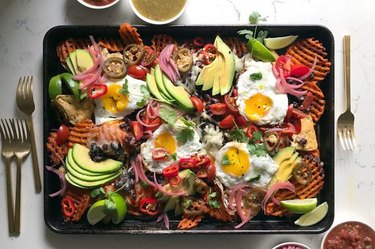Breakfast nachos with sweet potato waffle fries, black beans, shiitake bacon, and eggs on a baking dish.