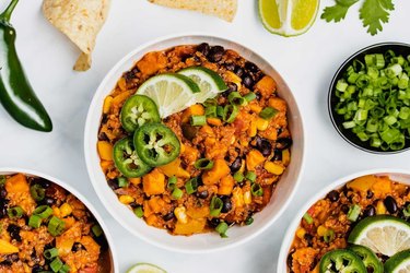 Instant Pot Vegan Chili in a white bowl on marble countertop next to ingredients like jalapeno peppers, lime and cilantro.